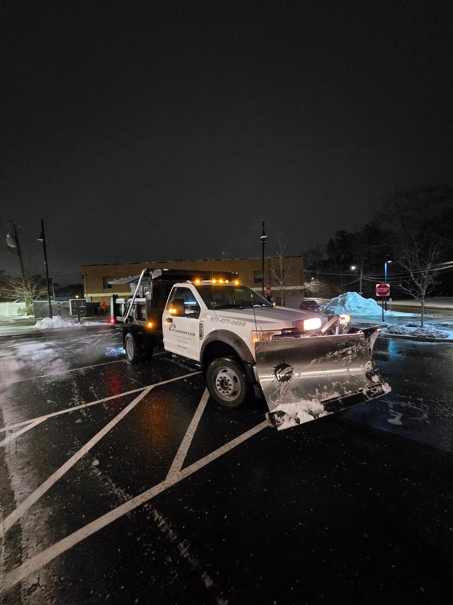 Snowplow in a parking lot at night, clearing snow. White truck with plow blade, dark sky.