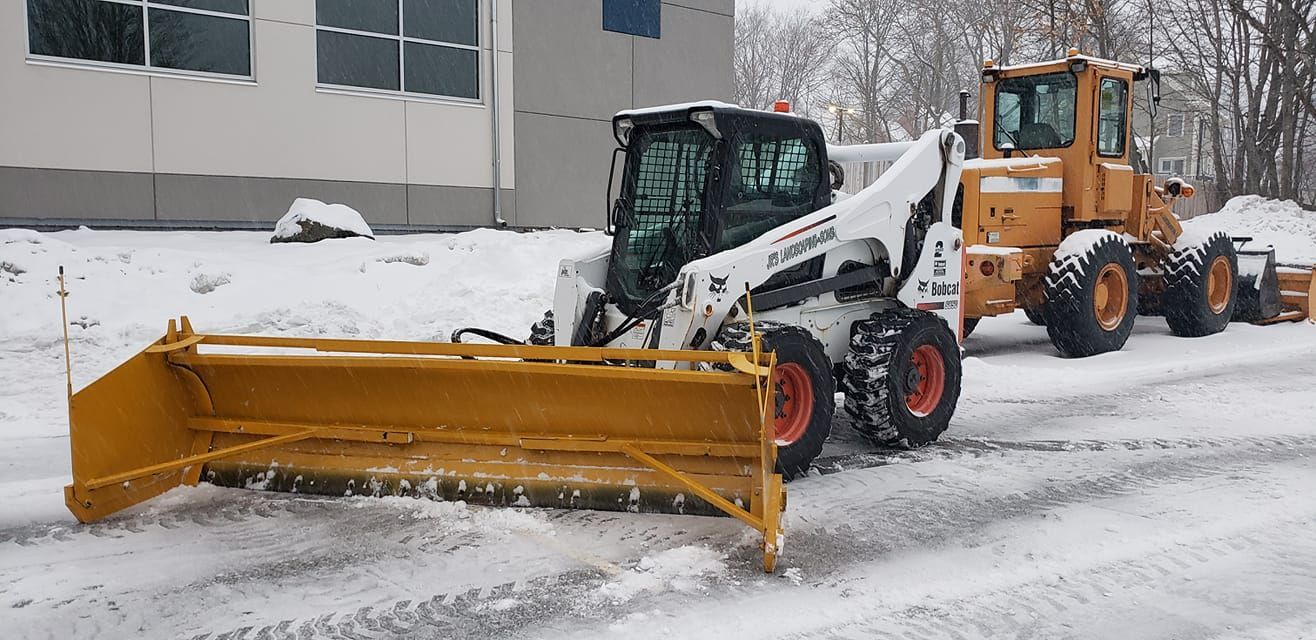 Two snow plows clearing snow from a road in front of a building. Bobcat commercial snow