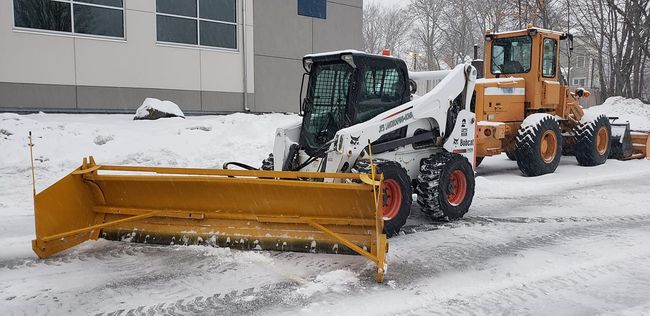 snow plow lifting snow into a dump truck for commercial snow removal.