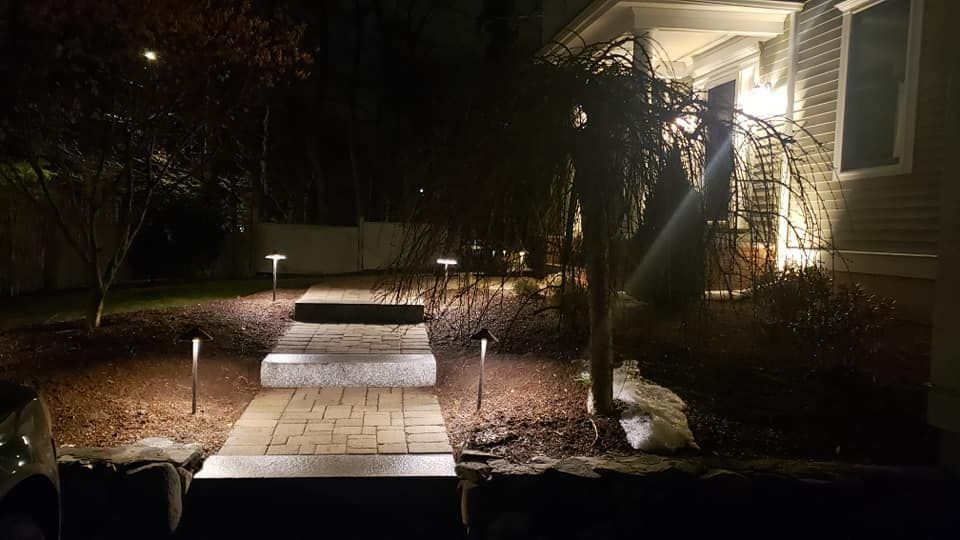 A paver walkway with illuminated new outdoor pathlights leads to a house entrance at night.