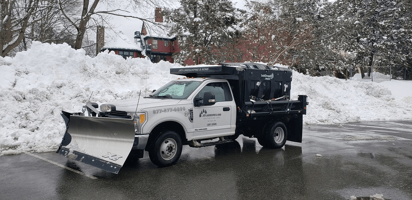 White snowplow truck clearing snow from a paved lot. A large pile of snow is behind the truck. Commercial snow and salting. 