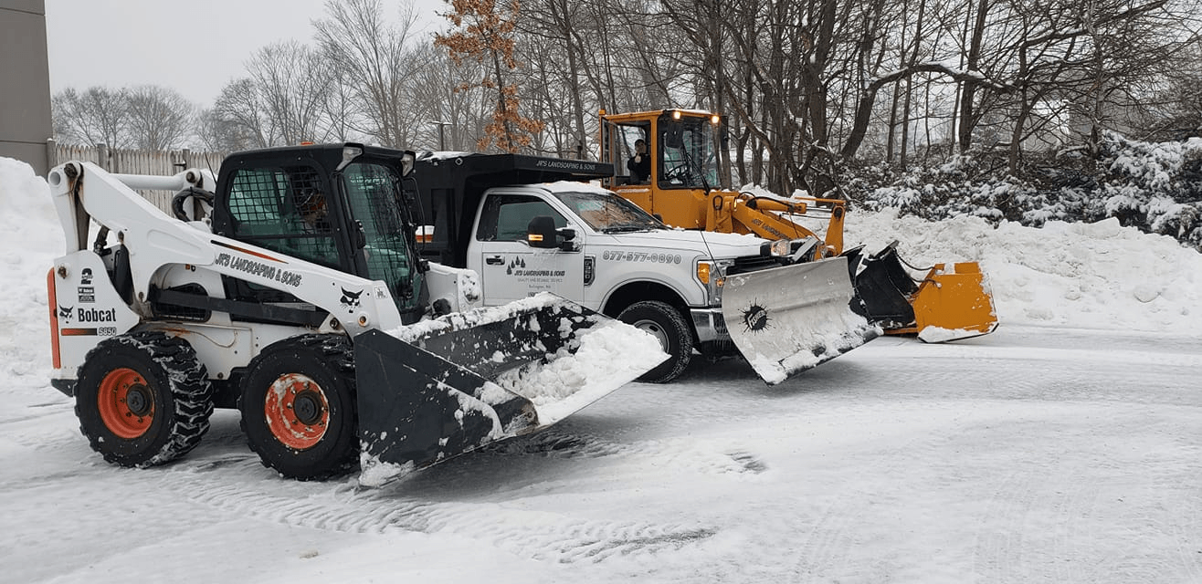 Snow removal equipment, a Bobcat, truck, and loader, clearing snow on a snowy day. Commercial lot