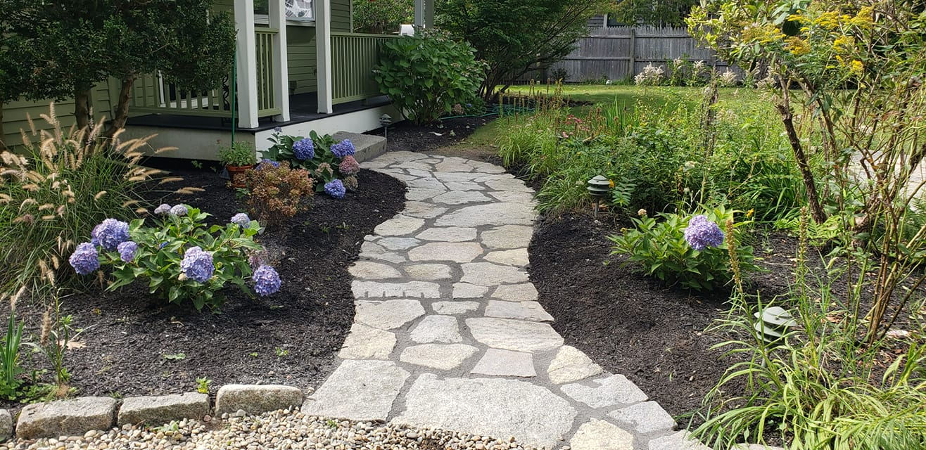Custom stone walkway winds through a garden of flowers and perennials leading to front porch. 