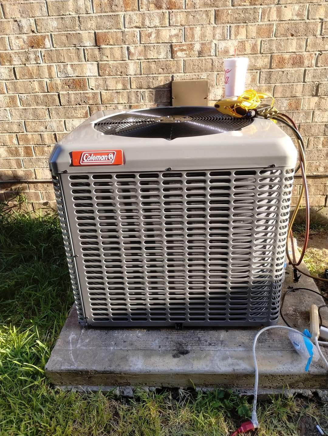 An air conditioner is sitting on top of a concrete block in front of a brick wall.
