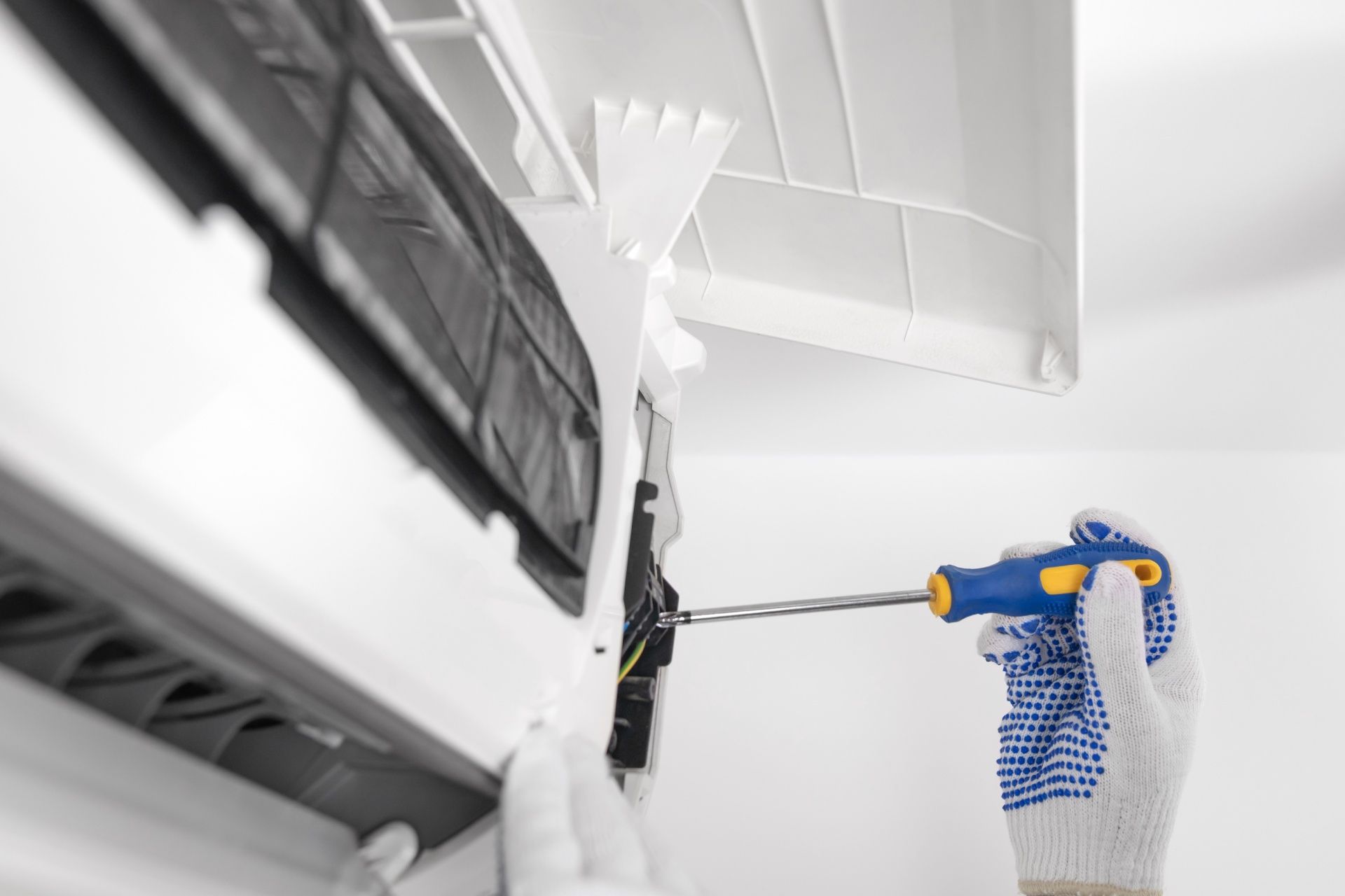 A person is fixing an air conditioner with a screwdriver.