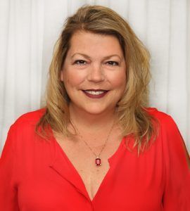 Woman in red blouse smiles, wearing pendant necklace.