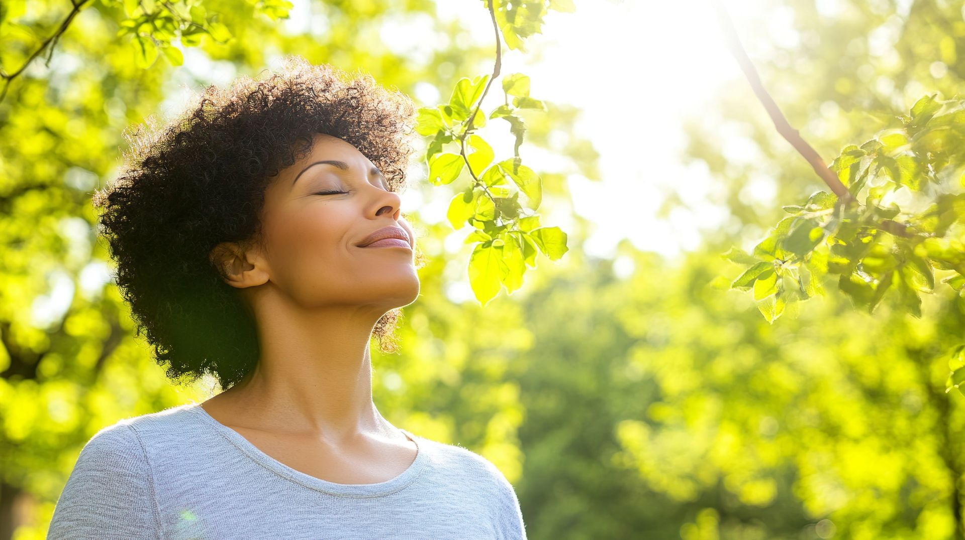 A woman is standing in a park with her eyes closed.