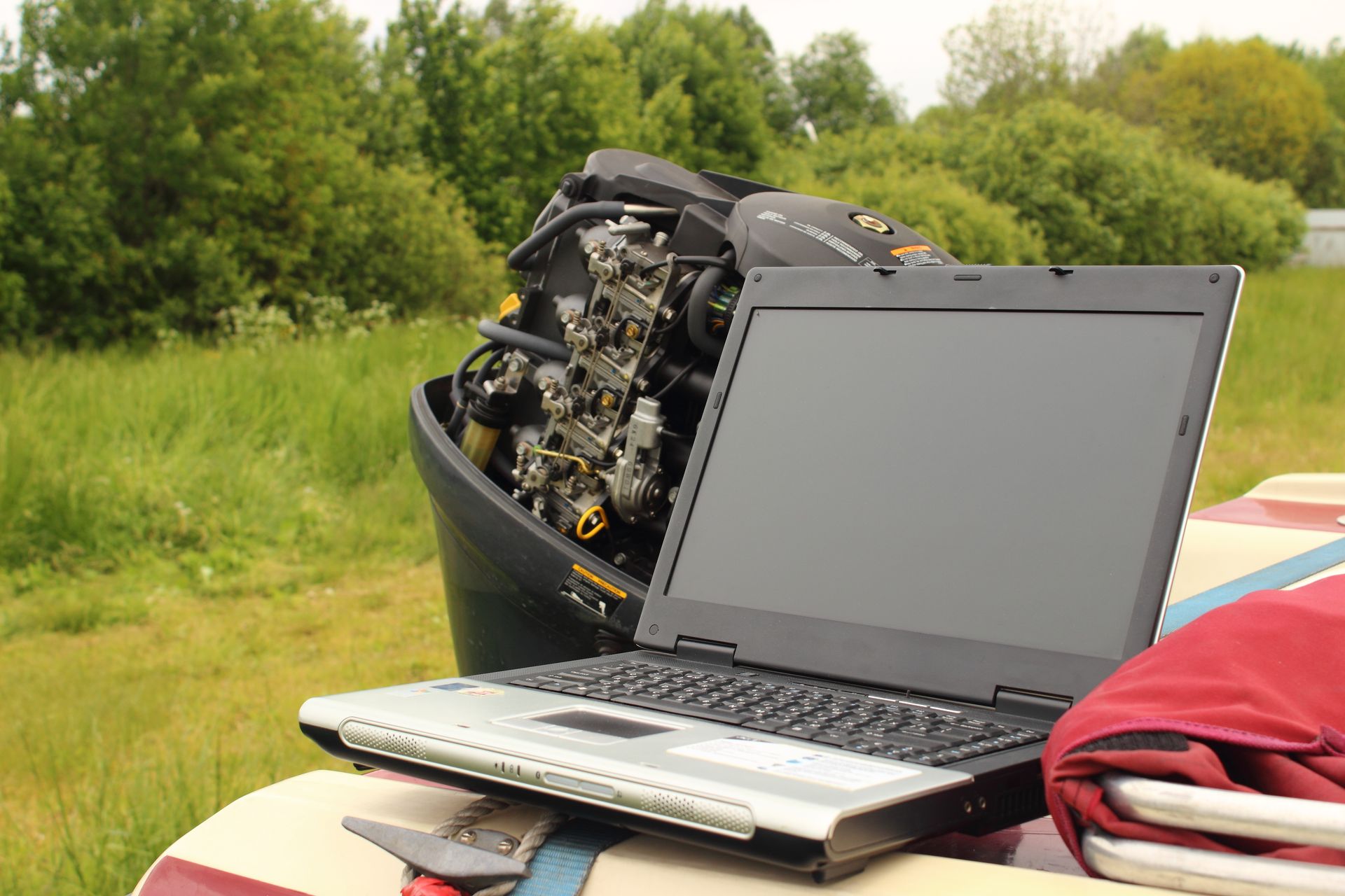 Laptop on a picnic table with an open engine behind it in a grassy outdoor setting