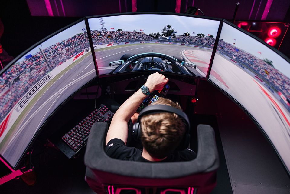 Person using a racing simulator with three curved screens and a steering wheel, viewed from behind