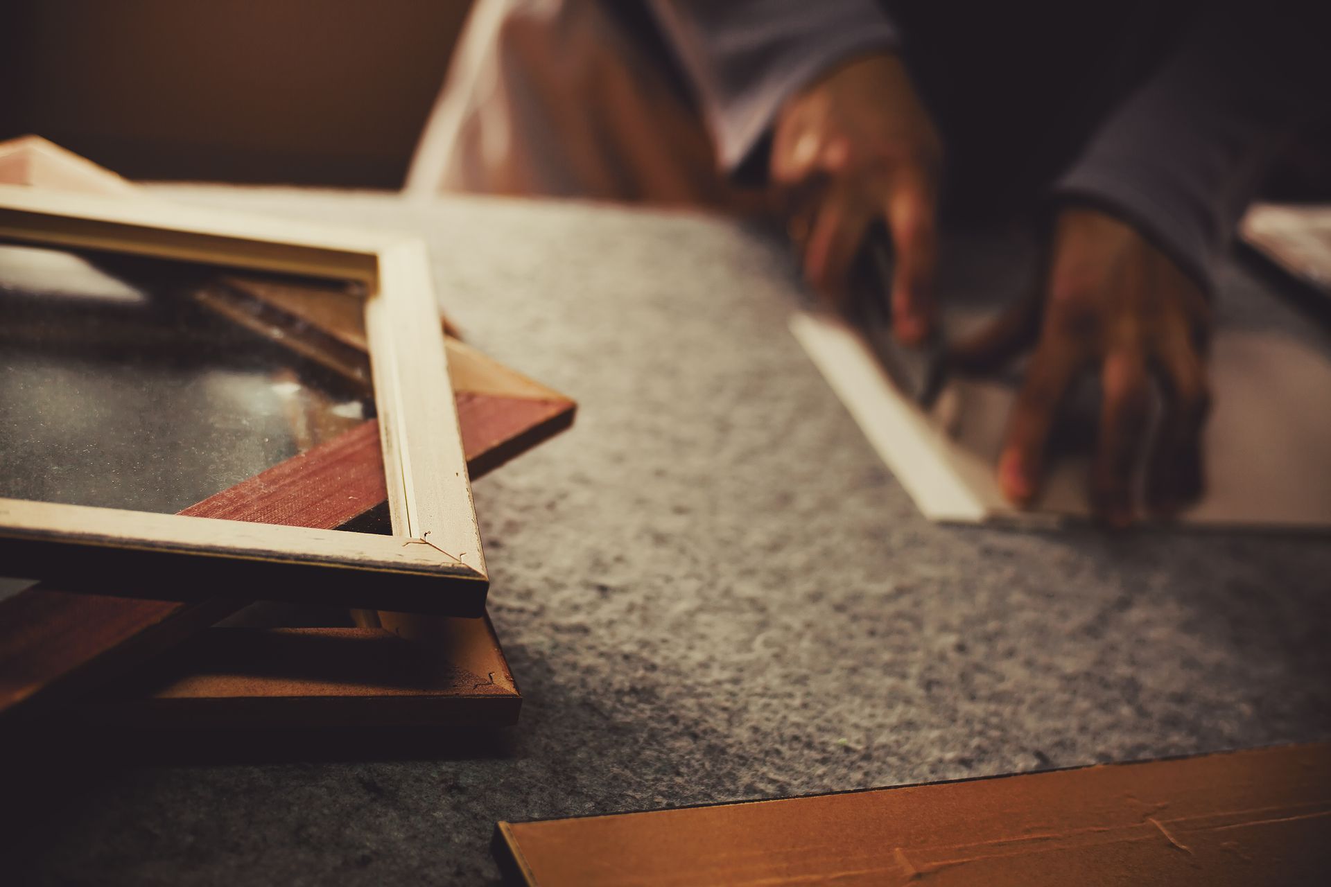 Hands assembling a wooden picture frame on a workbench beside stacked frame mouldings.