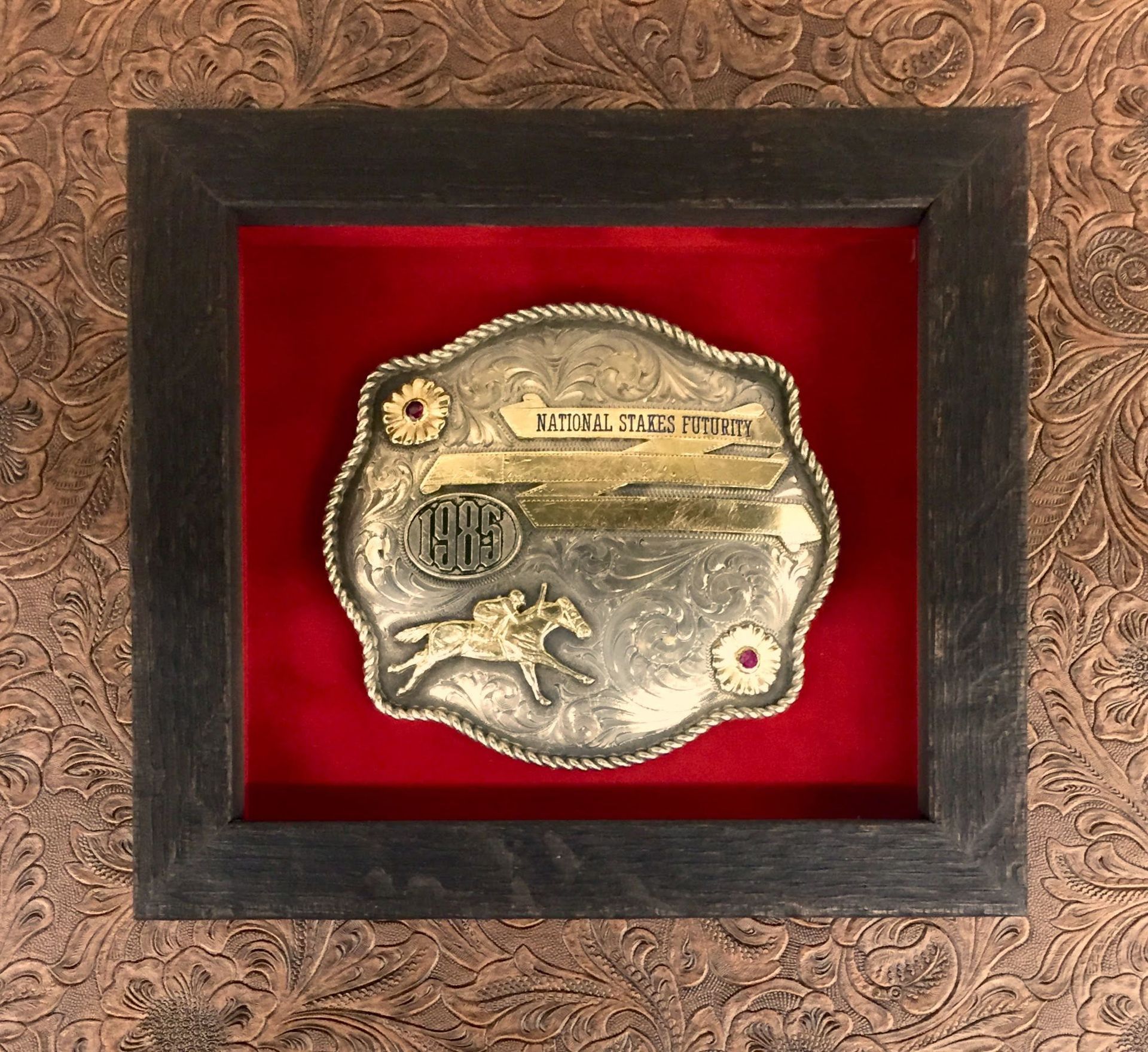 Framed rodeo belt buckle against red velvet, a 1968 National Finals Rodeo buckle.