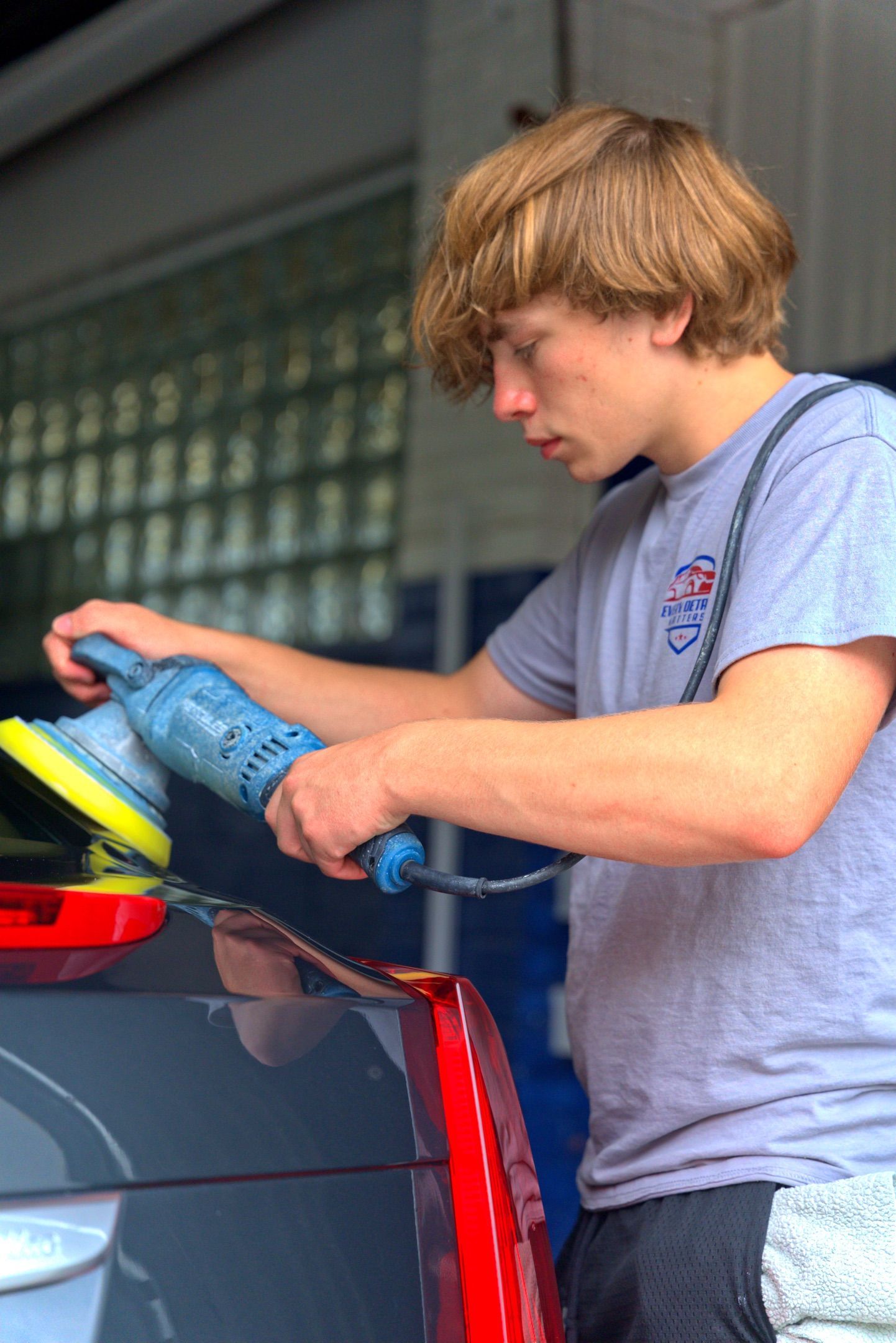 Person using a blue buffer to polish a car in a garage.