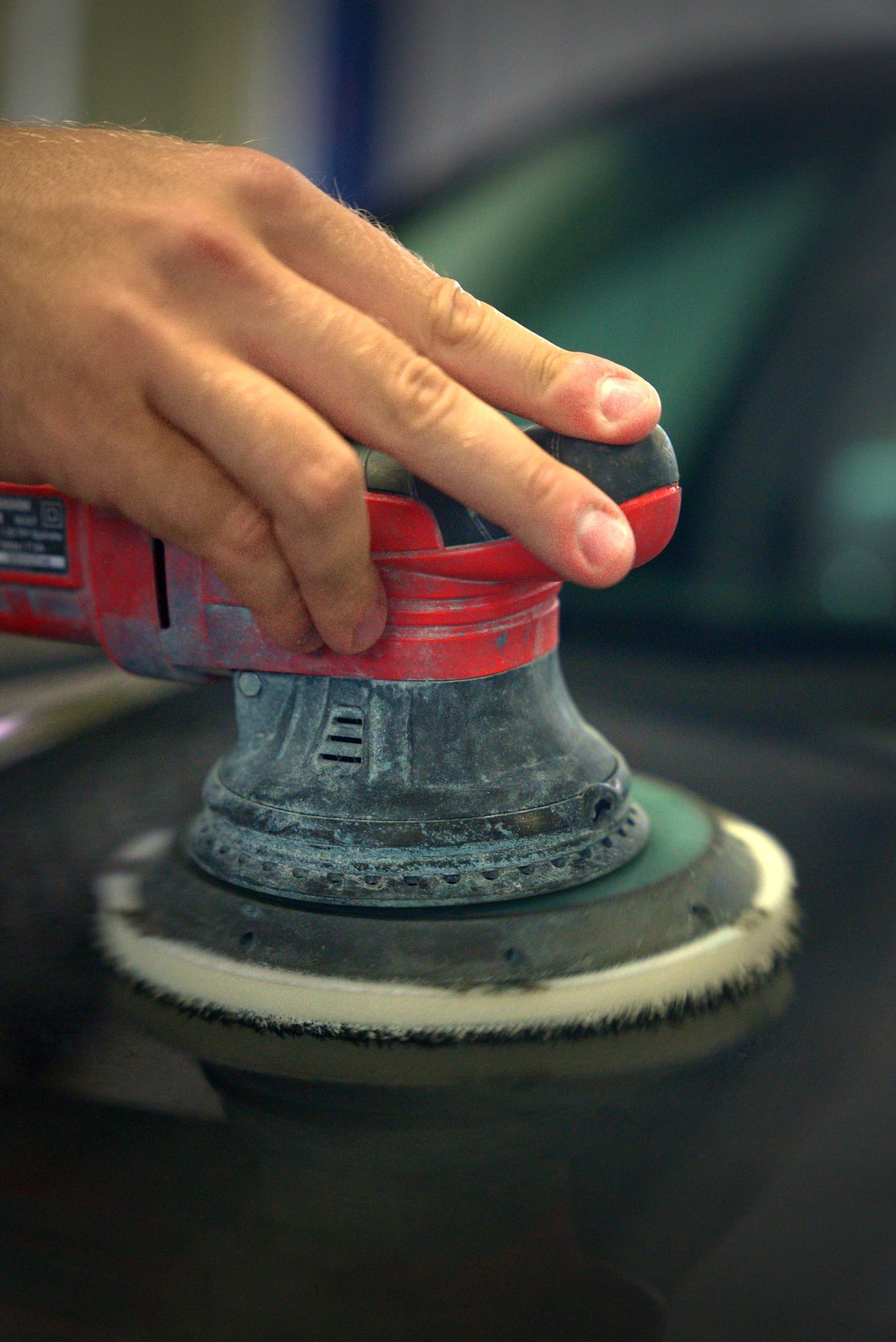 Hand holding a red polisher buffing a car surface
