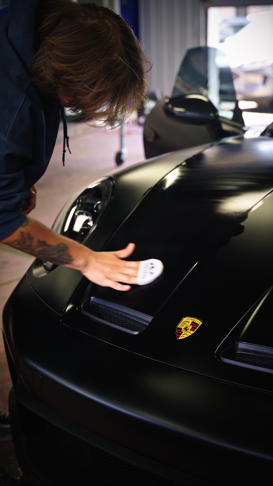 Person polishing a black Porsche car hood in a garage