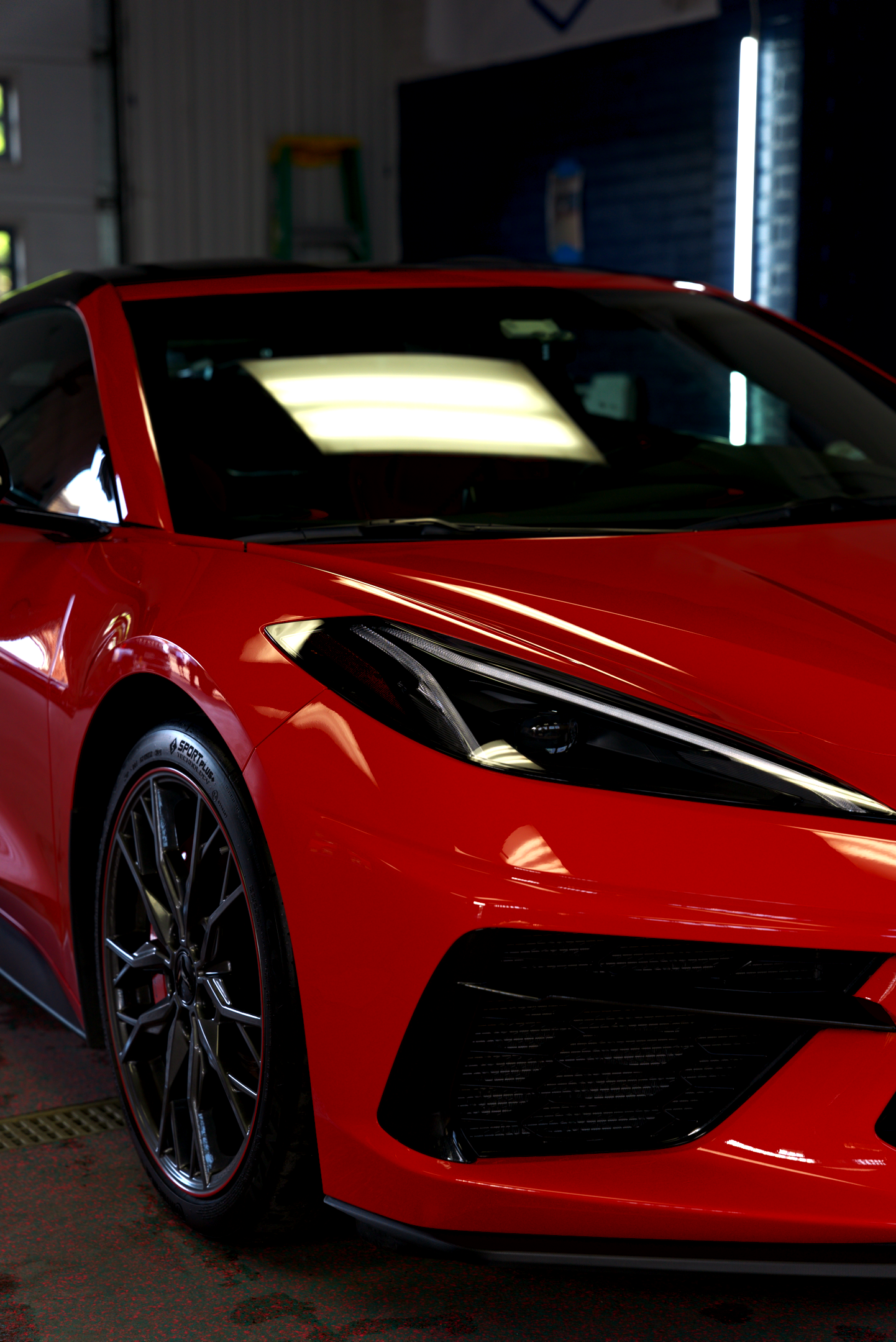 Red sports car in a dim garage, close-up on the front side with black wheels.