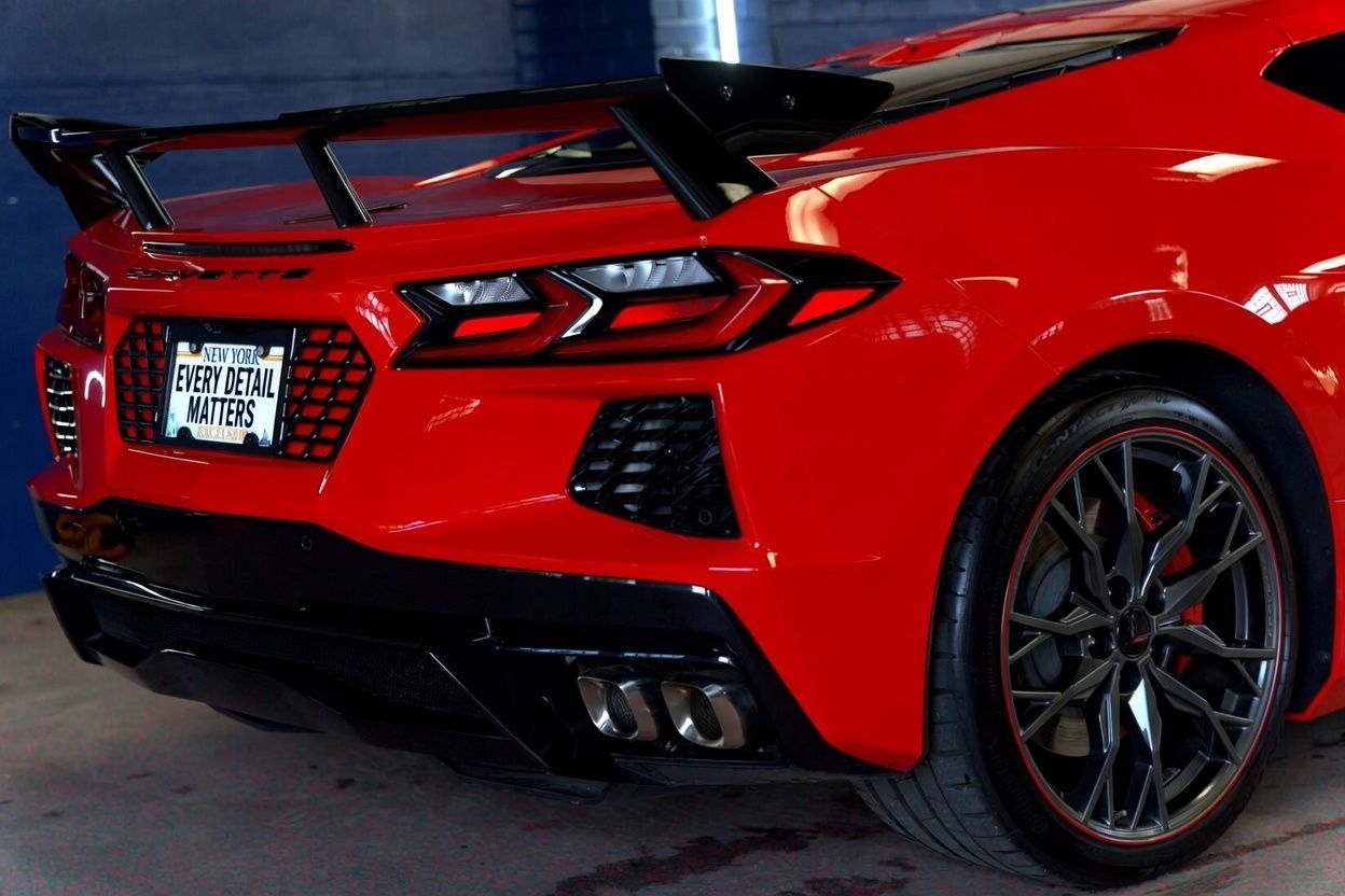 Red sports car rear quarter view with black spoiler and custom wheels in a garage