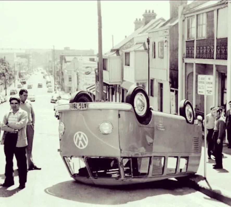 A vintage Volkswagen van is upside down on the street.