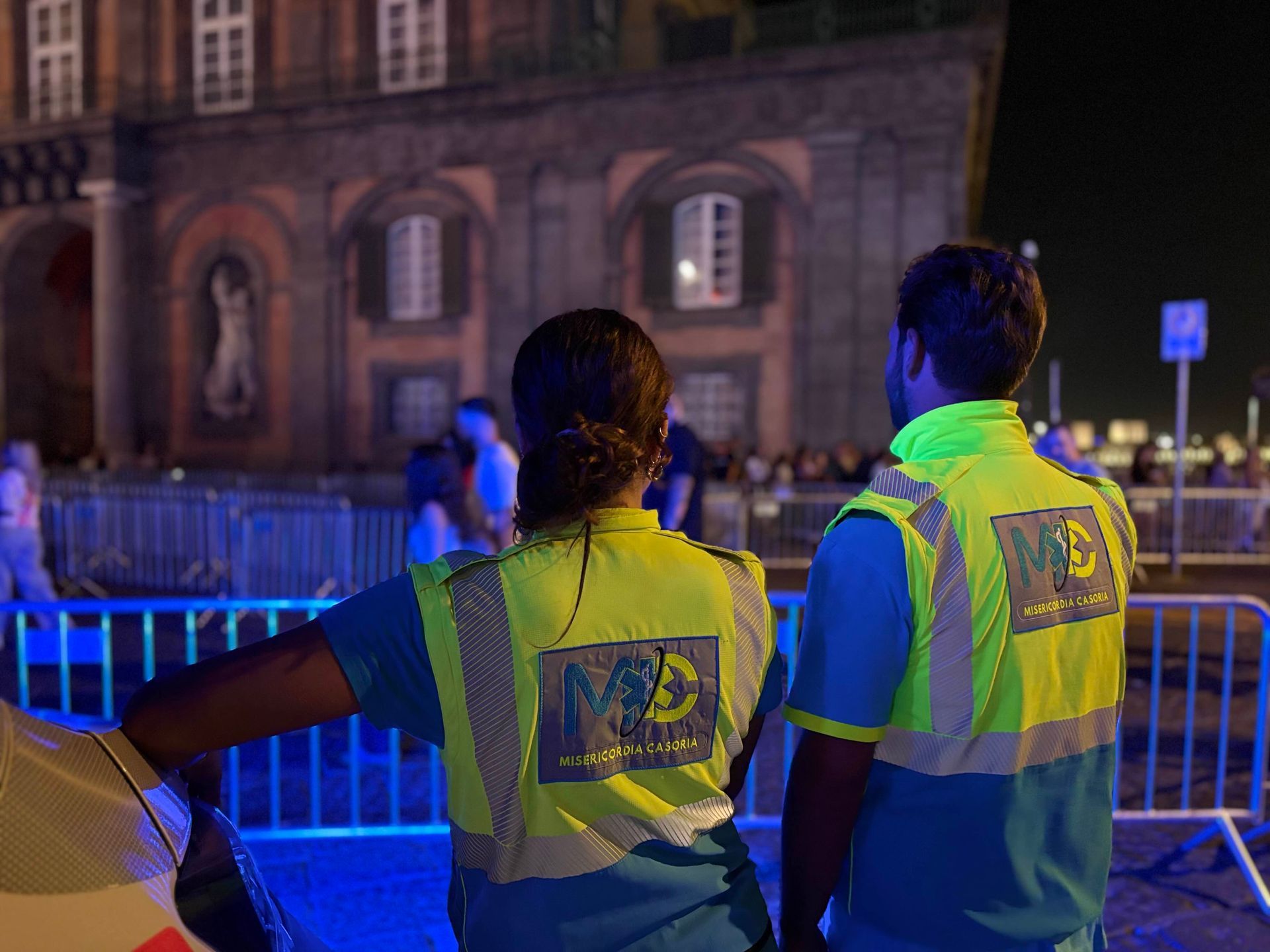 Due persone con giubbotti fluorescenti in piedi vicino a un edificio di notte.