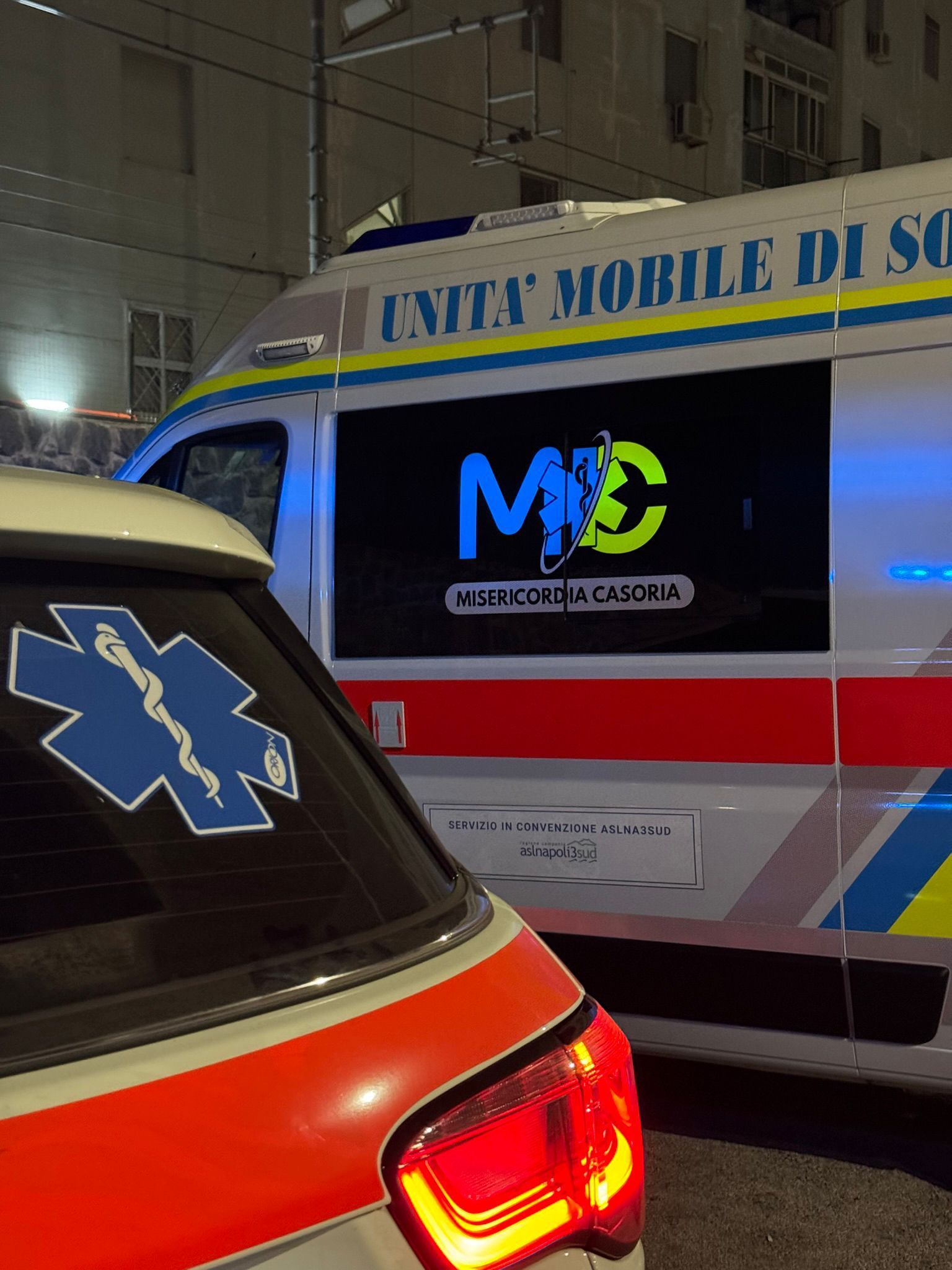 Veicoli di emergenza, tra cui un'ambulanza, parcheggiati di notte.