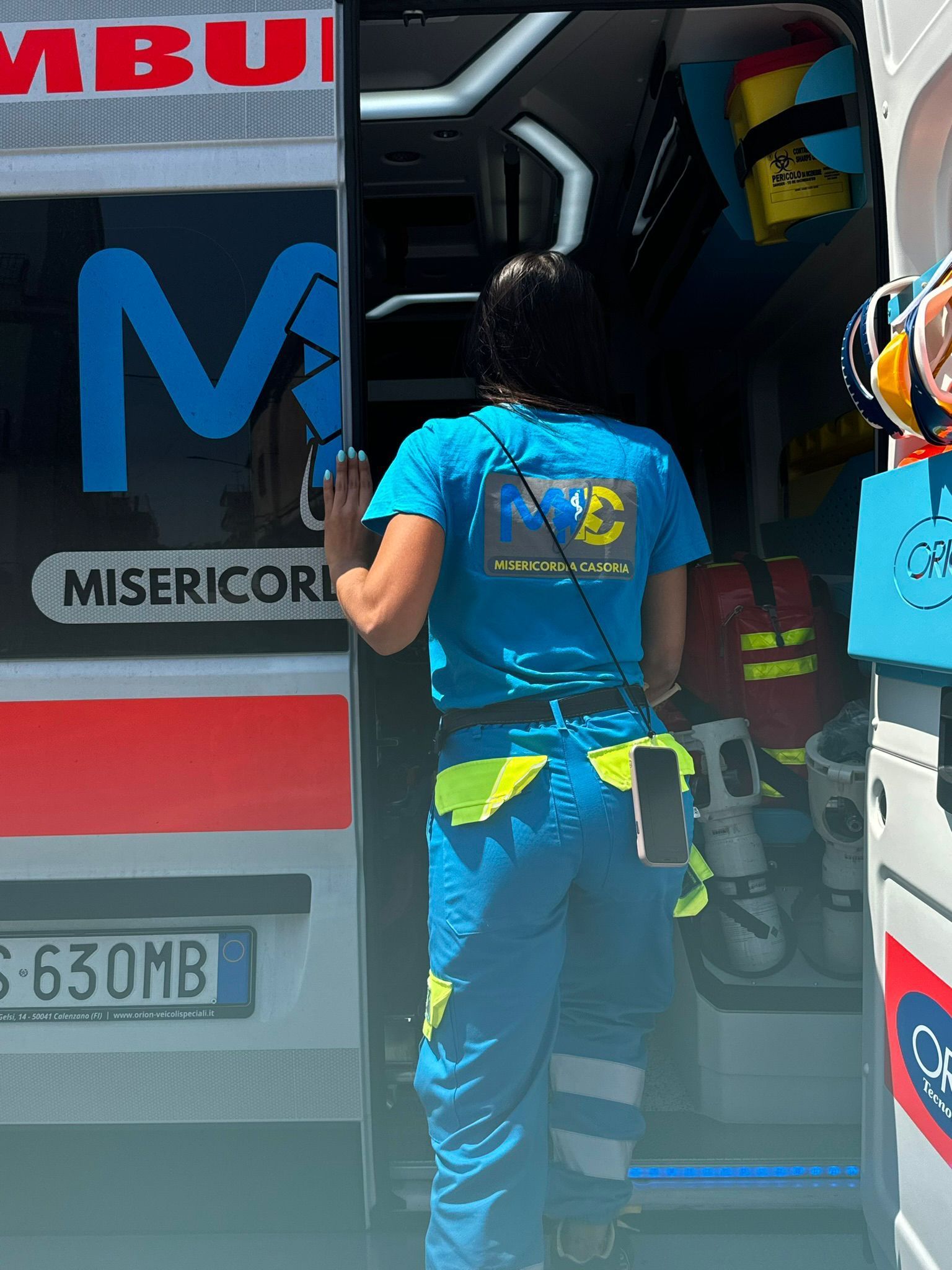 Persona in uniforme blu che entra in un'ambulanza, è visibile il logo 