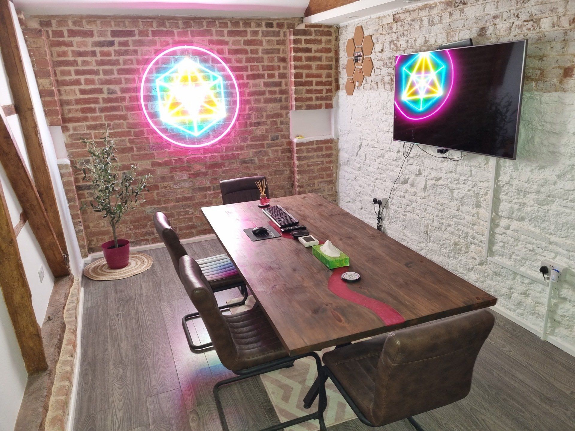 A conference room with a wooden table and chairs and a neon sign on the wall.