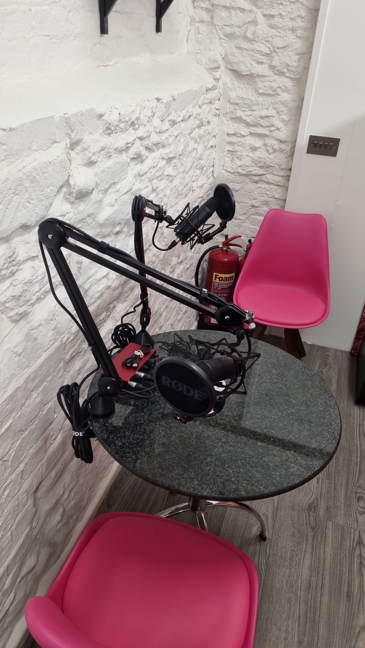 A microphone is sitting on top of a table next to two pink chairs.
