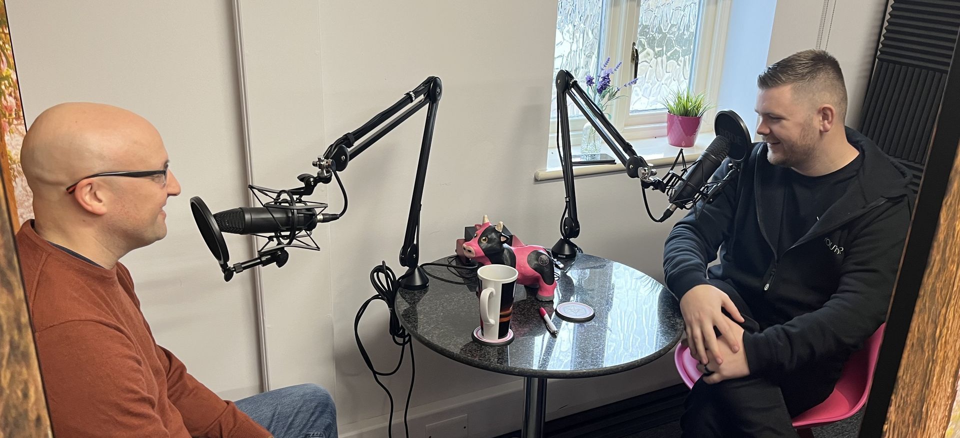 Two men are sitting at a table in front of microphones.