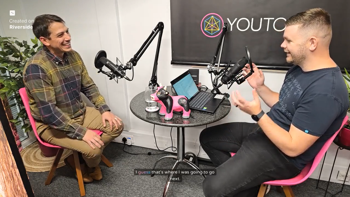 Two men are sitting at a table in front of a microphone.