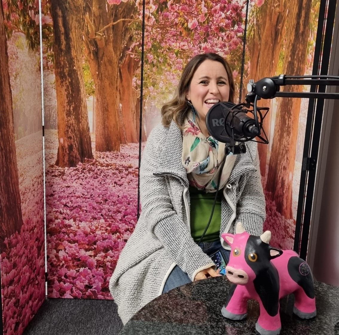 A woman is sitting in front of a microphone next to a stuffed cow.