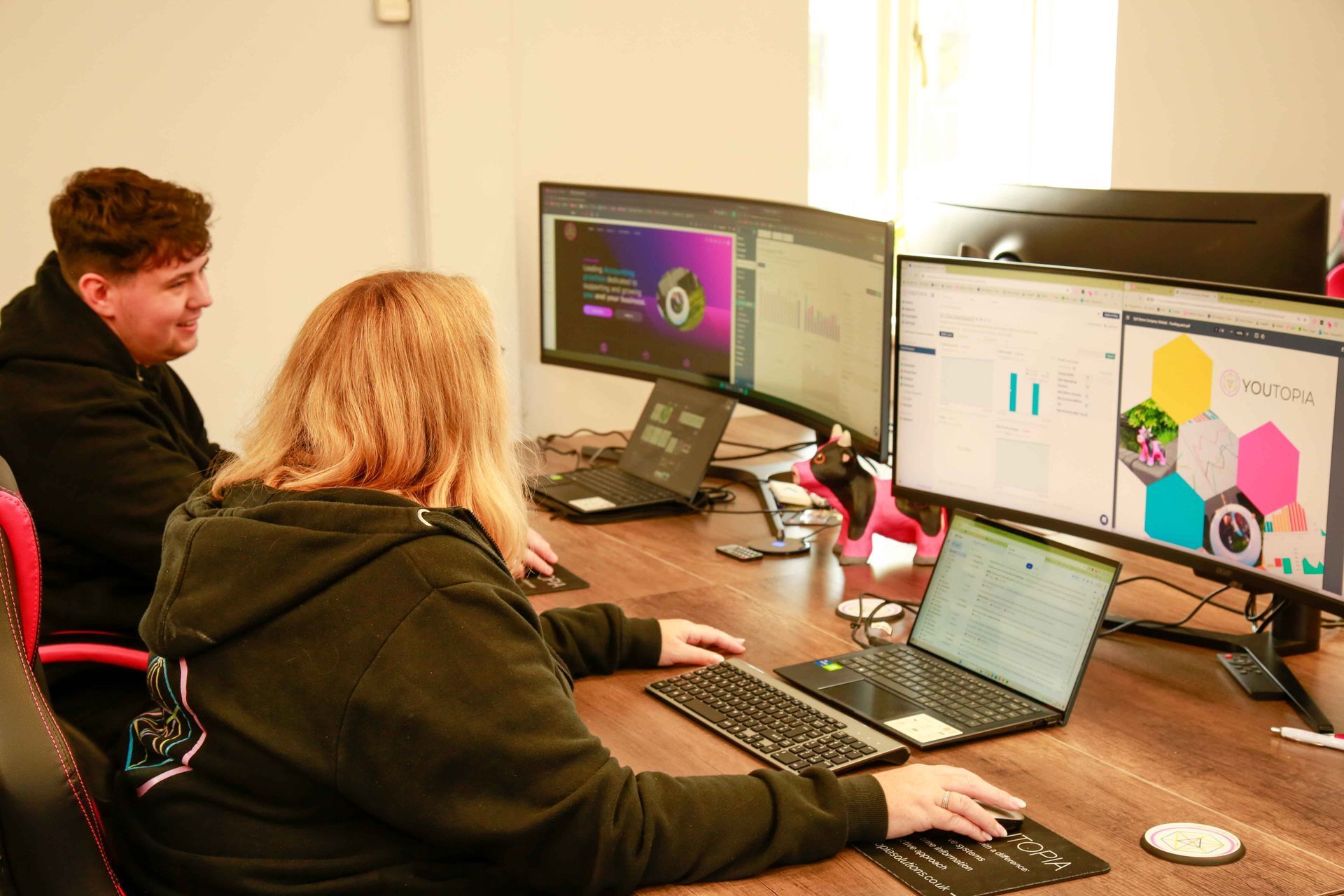 Two people working at a desk with multiple computer screens displaying data and graphics.