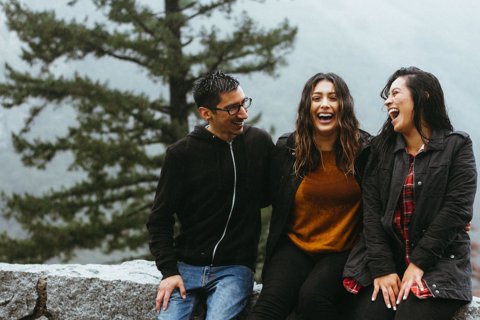 A group of people are sitting on a rock laughing.