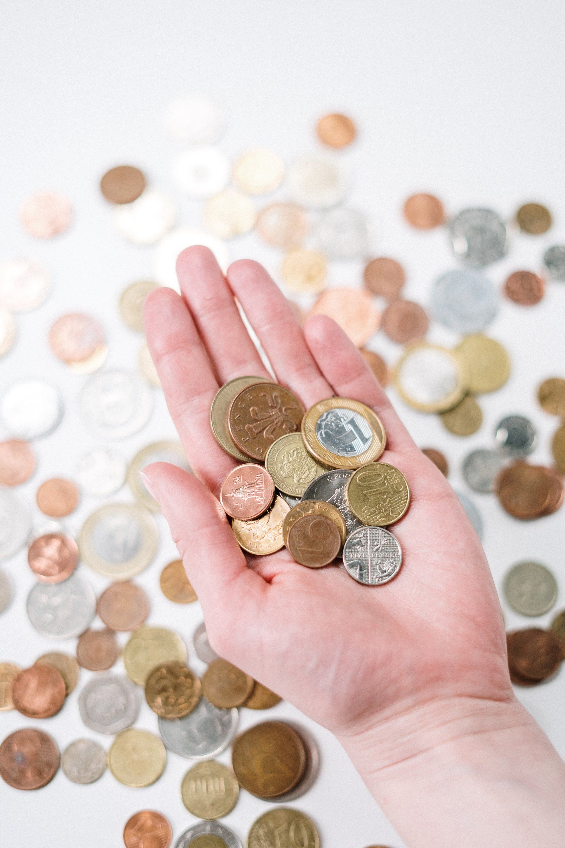 A person is holding a handful of coins in front of a pile of coins.