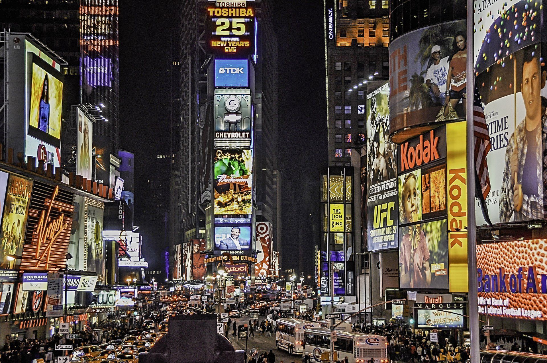 A busy city street at night with a kodak sign in the foreground