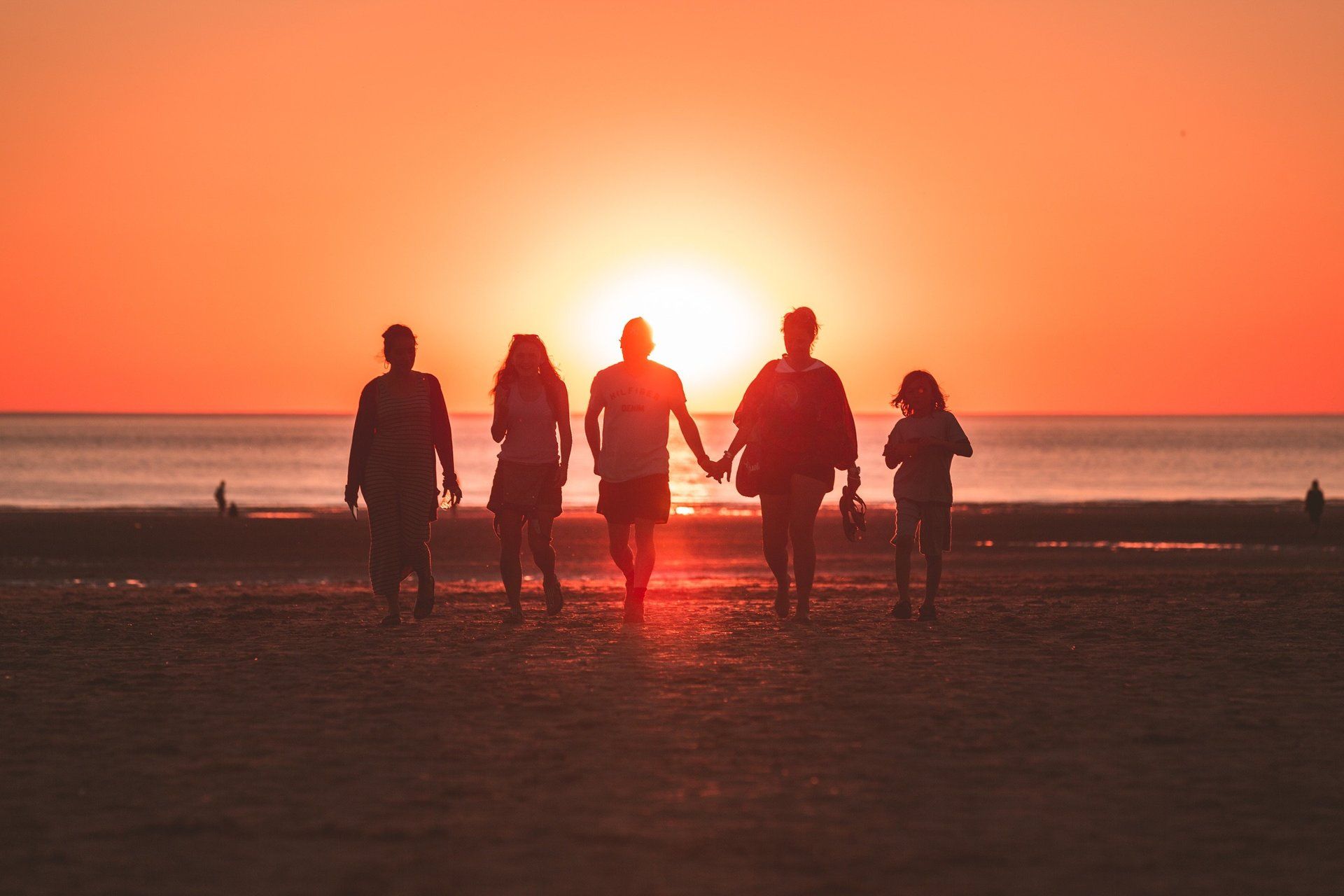 A group of people are walking on the beach at sunset holding hands.