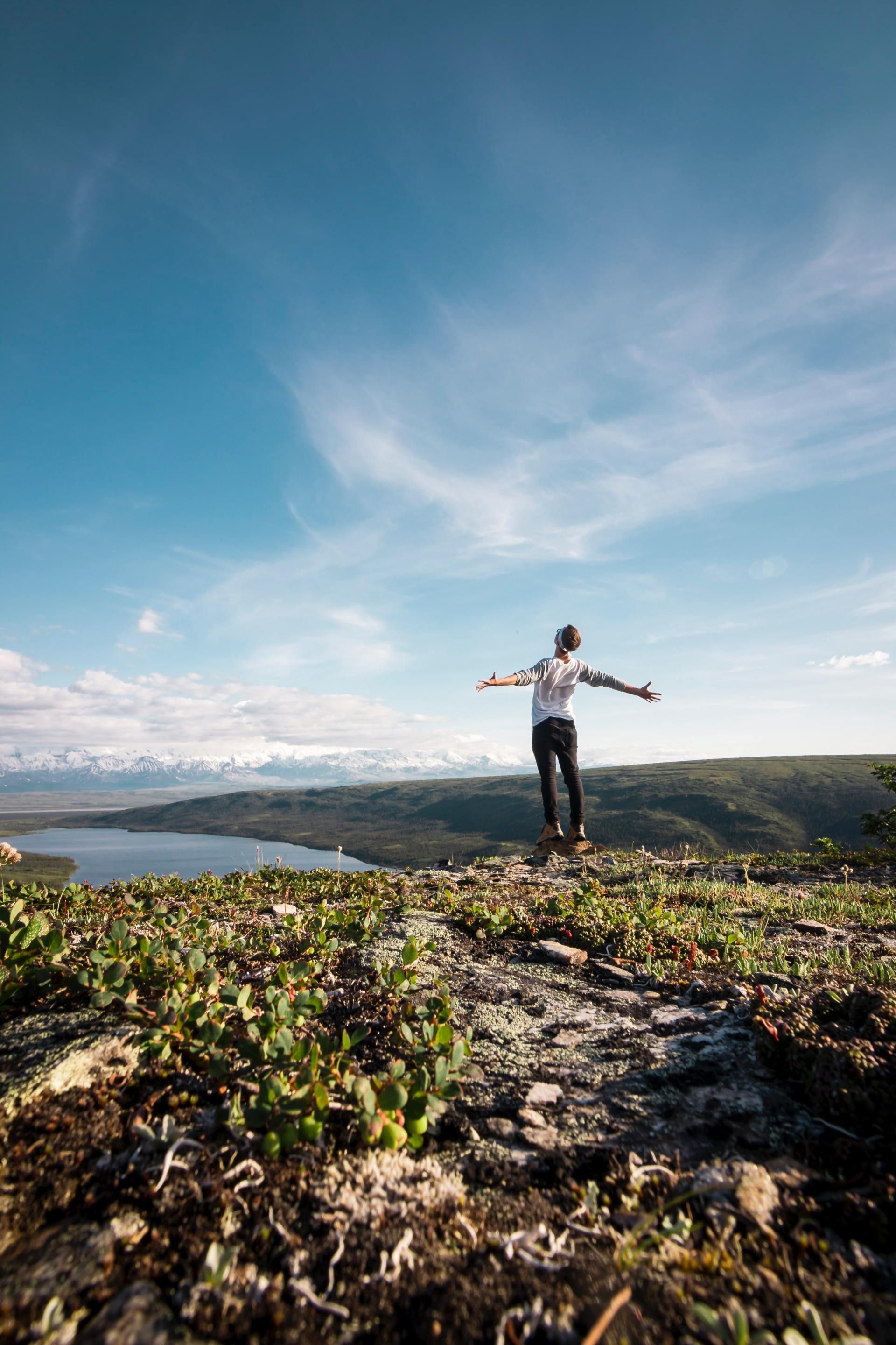 A man is standing on top of a hill with his arms outstretched.