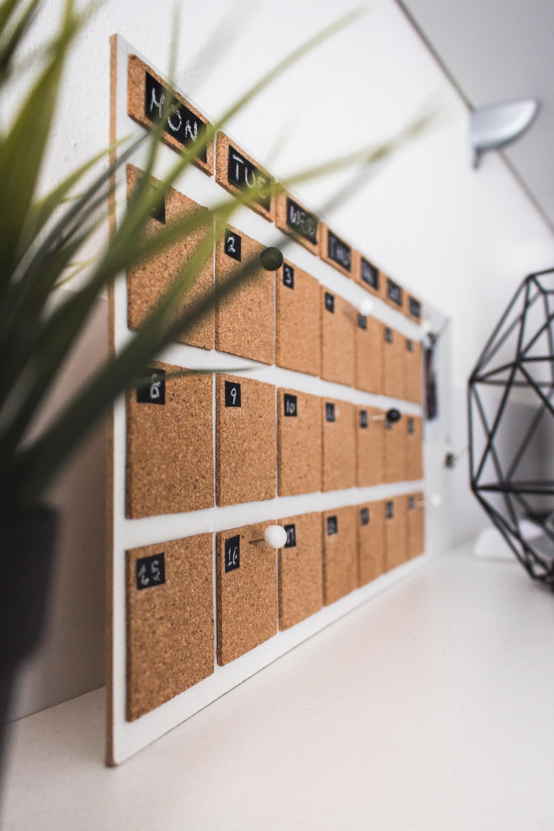 A calendar made of cork is sitting on a table next to a plant.