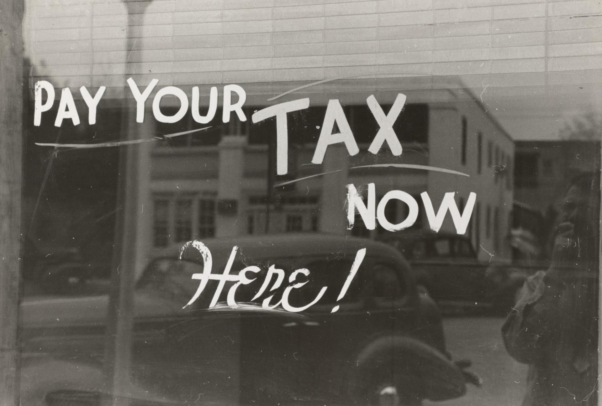A black and white photo of a sign that says pay your tax now here