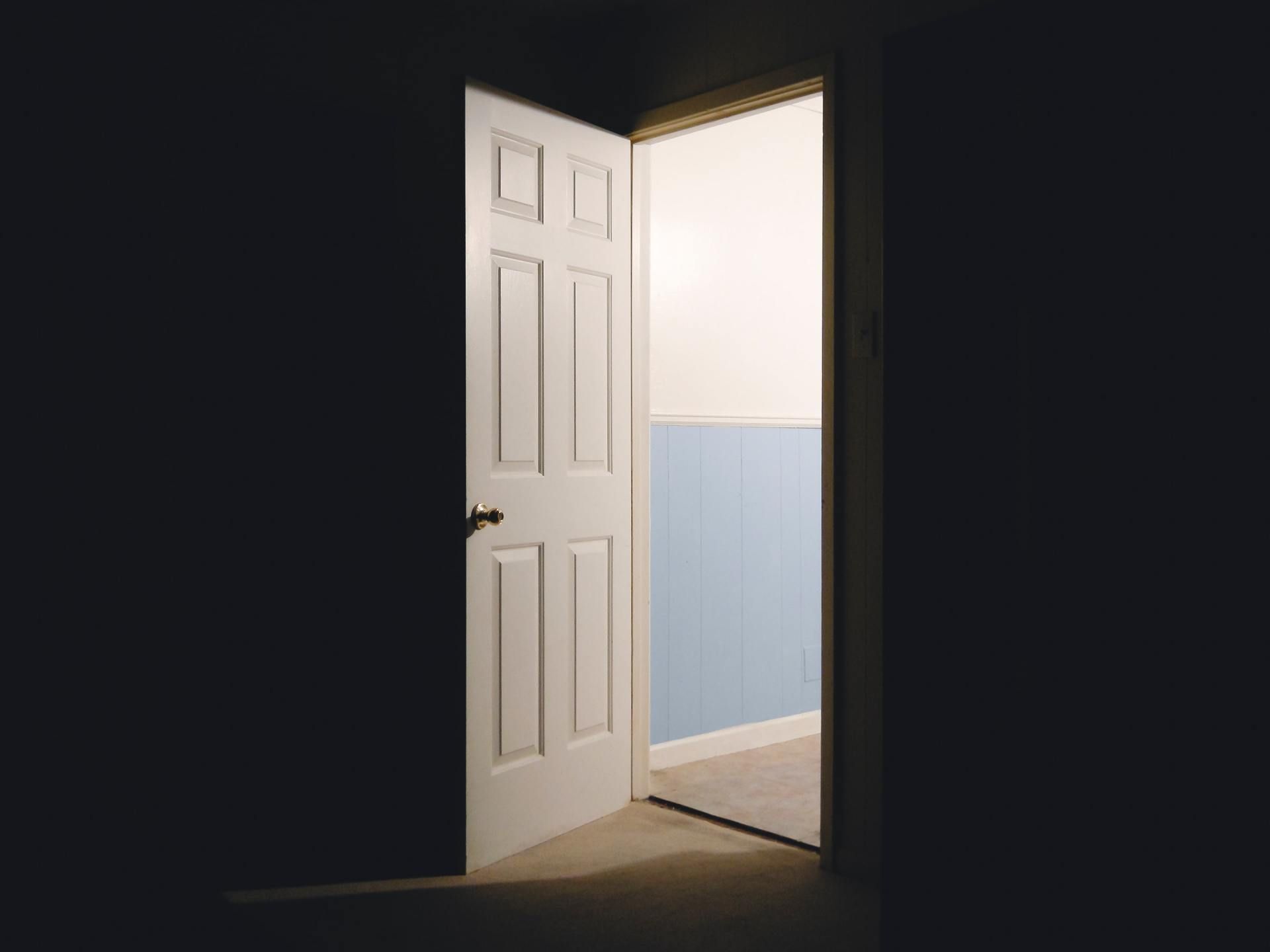 A light is shining through an open door in a dark room.