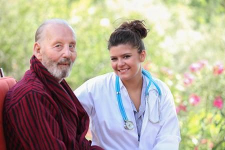 Two people smiling outdoors; one wears a white coat and stethoscope, the other a red shawl.