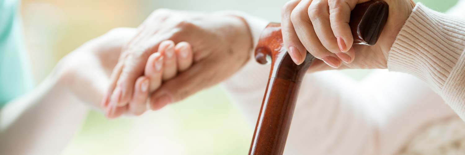 Hand resting on a wooden cane beside another hand in a soft, bright setting
