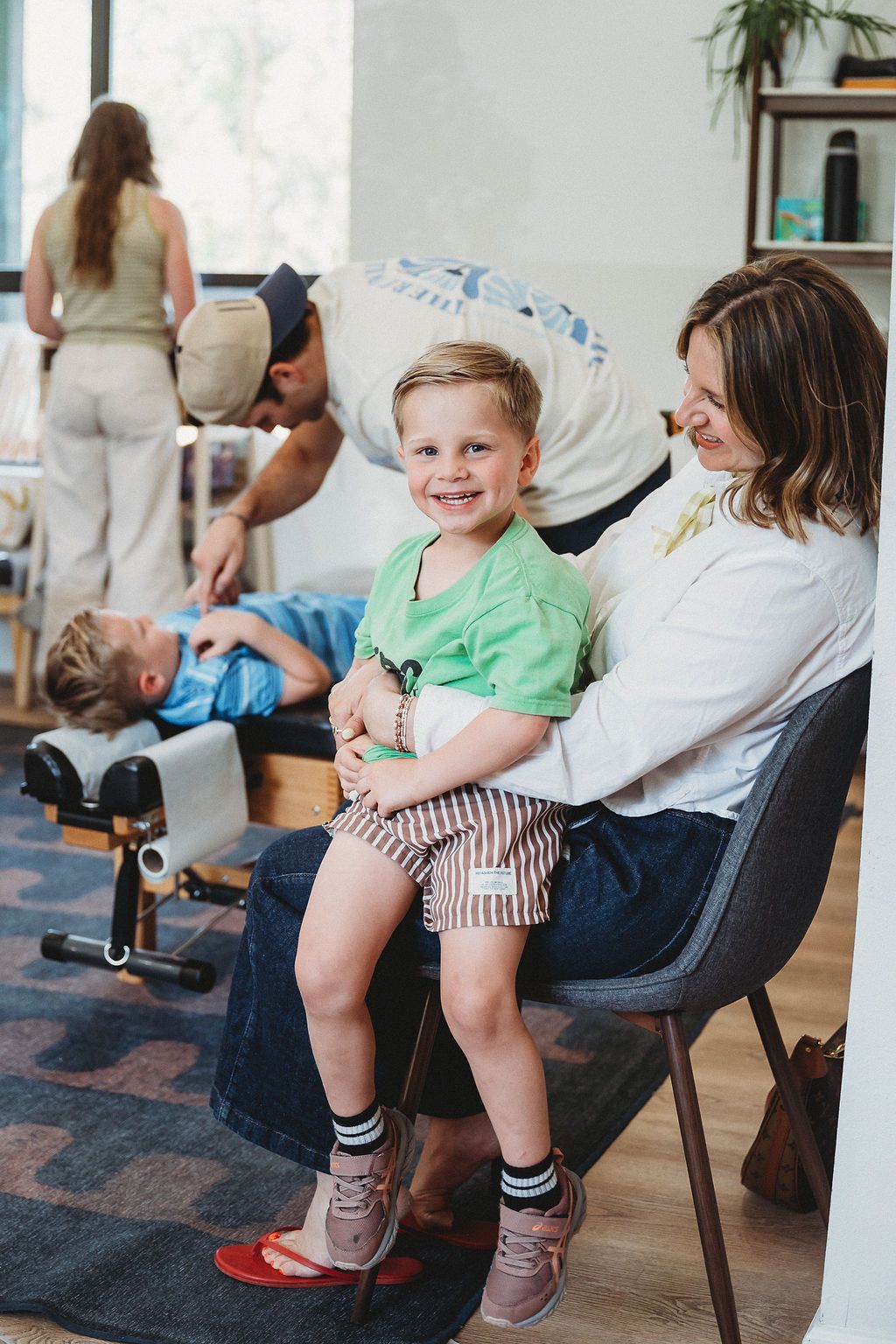 Child smiling on a chair while a woman sits beside him in a bright waiting room