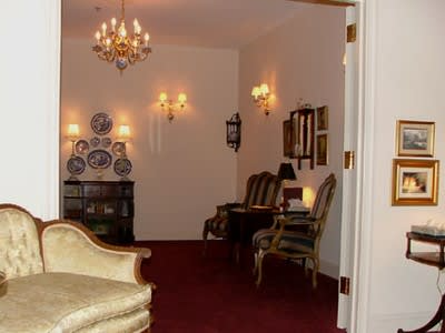 Elegant living room with red carpet, chandelier, wall sconces, and antique chairs