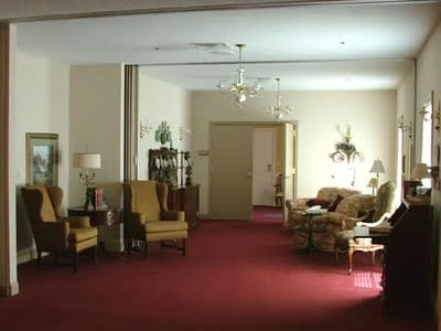 Elegant living room with red carpet, upholstered chairs, wall lamps, and a doorway at the back