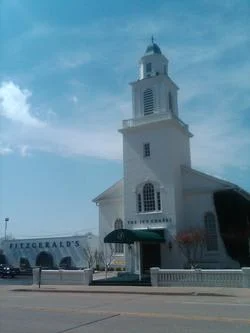 White church tower with a green awning beside a street under a blue sky
