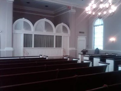 Empty church sanctuary with wooden pews, arched windows, and hanging chandeliers