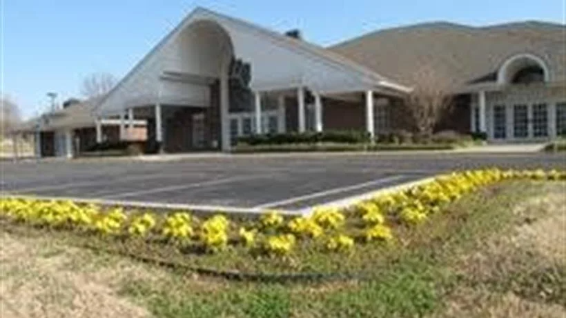 Brick building with arched entrance and yellow flowers along the curb under a cloudy sky