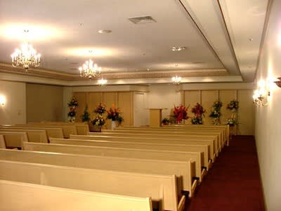 Empty church sanctuary with rows of wooden pews, chandeliers, and floral arrangements near the altar.