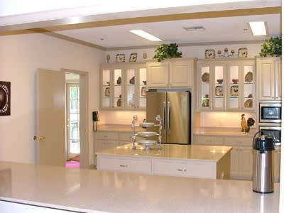 Bright kitchen with cream cabinets, stainless fridge, island sink, and coffee maker.