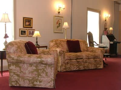 Cozy living room with floral armchairs, red carpet, wall art, and lamps lit along the walls