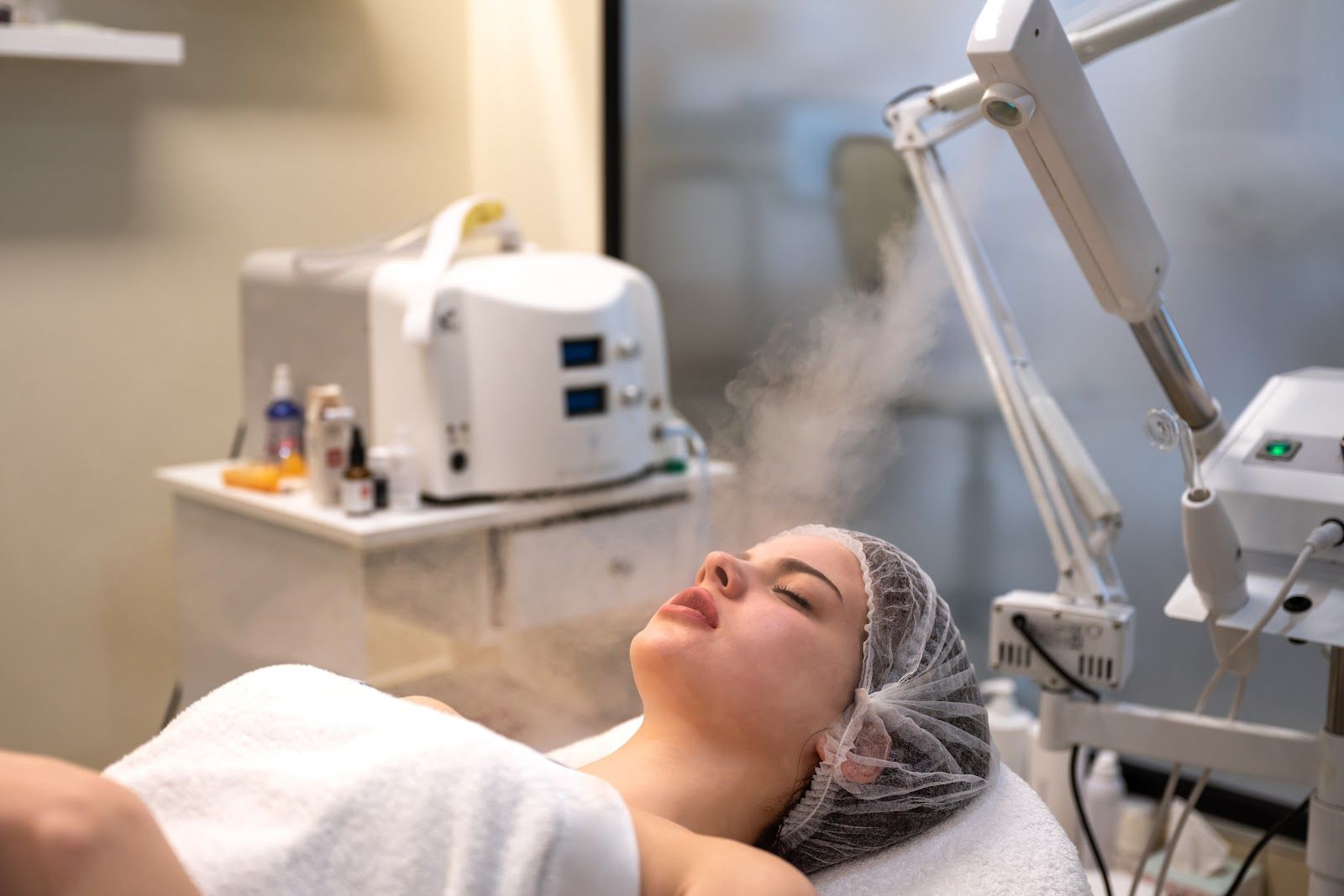 Person receiving a facial steam treatment in a spa, lying back as steam rises from a machine.